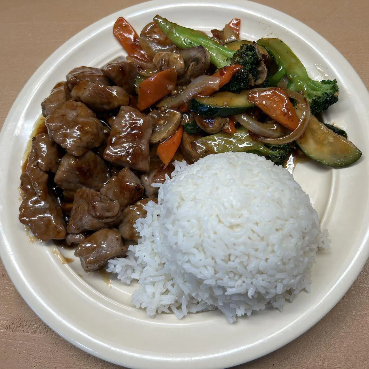 Beef Vegetable Rice Plate shows a serving of white rice accompanied by tender beef pieces and a mix of stir - fried vegetables like broccoli, zucchinis, mushrooms, onions, and carrots, all coated in a savory sauce at Asian Wok, a Chinese restaurant in Port Lavaca