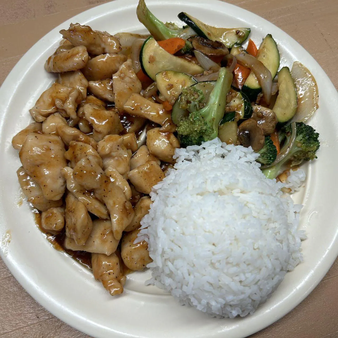 Chicken Vegetable Rice Plate shows a serving of white rice accompanied by tender chicken pieces and a mix of stir - fried vegetables like broccoli, zucchinis, mushrooms, and carrots, all coated in a savory sauce at Asian Wok, a Chinese restaurant in Port Lavaca